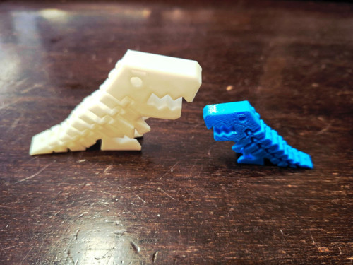 Dos dinosaurios, uno blanco más grande y otro azul más pequeño, impresos con resina en 3D