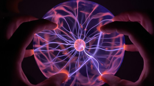 Unas manos frente a una bola de plasma de luz rosada. 