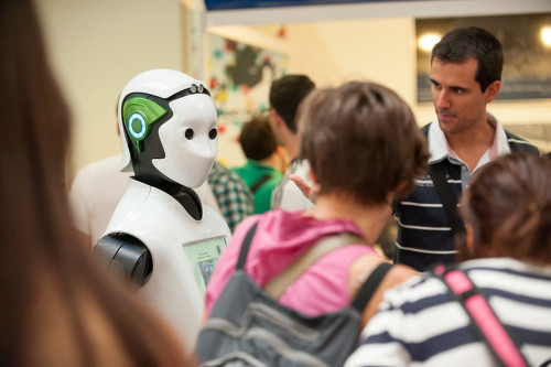 Un profesor muestra un robot blanco humanoide a dos alumnos de secundaria.