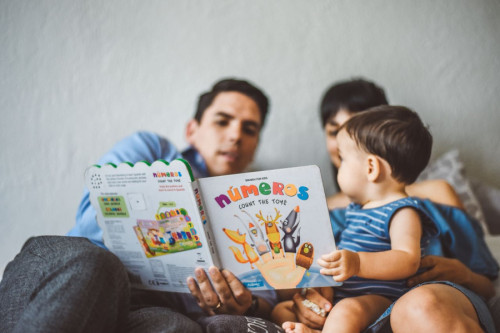 Un padre y una madre le enseñan a una bebé un libro de cuentos sobre números y juguetes llamado Count the toys
