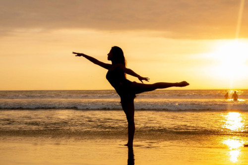 Una bailarina de ballet ejecuta un movimiento en la orilla del mar al atardecer