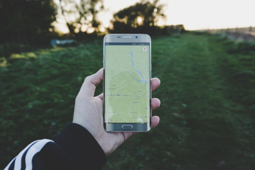 Un móvil muestra una app de mapa y ubicación a un chico que está en el campo